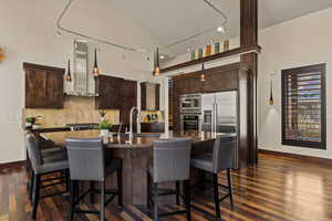 Kitchen featuring dark brown cabinetry, sink, stainless steel appliances, a kitchen island with sink, and wall chimney range hood