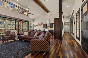 Living room with beamed ceiling, ceiling fan, dark hardwood / wood-style flooring, and high vaulted ceiling