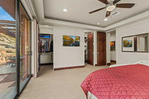 Carpeted bedroom with ceiling fan, a walk in closet, a raised ceiling, and a closet