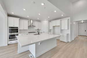 Kitchen with backsplash, visible vents, a sink, double oven, and wall chimney exhaust hood
