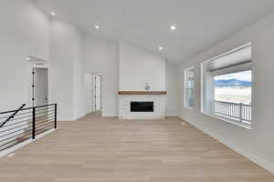 Unfurnished living room featuring a stone fireplace, baseboards, high vaulted ceiling, light wood finished floors, and recessed lighting