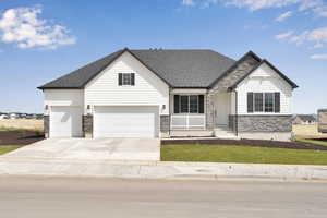 View of front of property with roof with shingles, a front yard, driveway, and stone siding