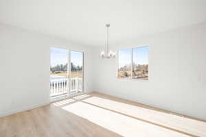 Unfurnished room featuring an inviting chandelier, a healthy amount of sunlight, and light hardwood / wood-style floors