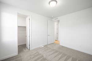 Unfurnished bedroom featuring light colored carpet, a closet, and a walk in closet