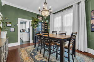 Dining space with ornamental molding, dark wood-type flooring, a wealth of natural light, and an inviting chandelier