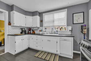 Kitchen featuring stainless steel range oven, sink, white cabinetry, tasteful backsplash, and white dishwasher