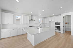 Kitchen with built in microwave, wall chimney exhaust hood, gas stovetop, stainless steel oven, and a kitchen island with sink