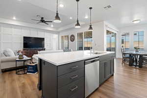 Kitchen featuring decorative light fixtures, sink, a kitchen island with sink, stainless steel dishwasher, and light wood-type flooring