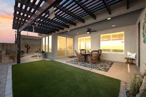 Patio terrace at dusk featuring ceiling fan, a yard, and a pergola