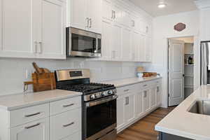 Kitchen featuring white cabinetry, backsplash, stainless steel appliances, and dark hardwood / wood-style floors