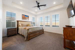 Carpeted bedroom with ceiling fan and a tray ceiling