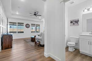 Bathroom with toilet, vanity, a tray ceiling, ceiling fan, and hardwood / wood-style floors