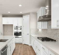 Kitchen with appliances with stainless steel finishes, white cabinetry, sink, hardwood / wood-style flooring, and wall chimney range hood