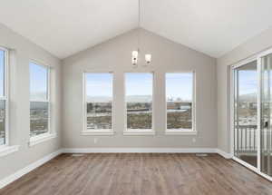 Interior space with an inviting chandelier, wood-type flooring, vaulted ceiling, and a healthy amount of sunlight