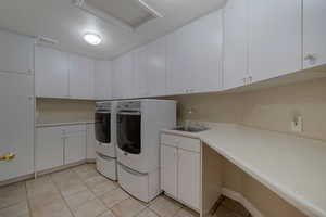 Laundry area with sink, cabinets, washer and dryer, and light tile patterned flooring