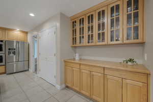 Kitchen featuring light tile patterned flooring, double wall oven, light oak cabinetry, and stainless steel fridge with ice dispenser