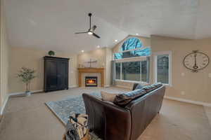 Carpeted living room with ceiling fan, lofted ceiling, a textured ceiling, and a fireplace