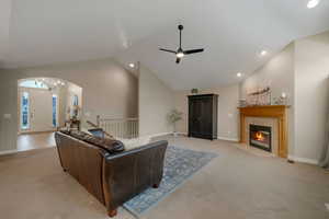 Living room with a premium fireplace, ceiling fan with chandelier, light colored carpet, and high vaulted ceiling