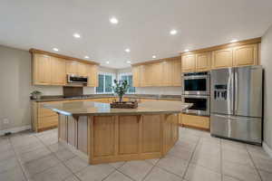 Kitchen with stainless steel appliances, a center island, light oak cabinets, and a kitchen breakfast bar