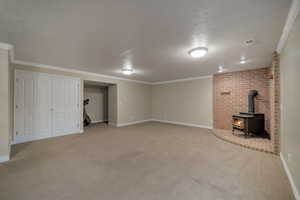 Basement with ornamental molding, light colored carpet, a textured ceiling, and a wood stove