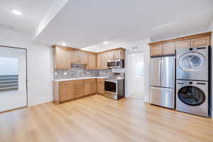 Kitchen with sink, backsplash, stainless steel appliances, stacked washer / drying machine, and light hardwood / wood-style floors