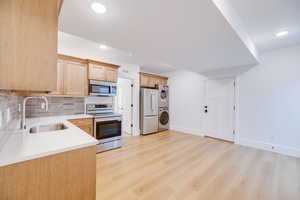 Kitchen with stacked washer and dryer, sink, light hardwood / wood-style flooring, appliances with stainless steel finishes, and tasteful backsplash