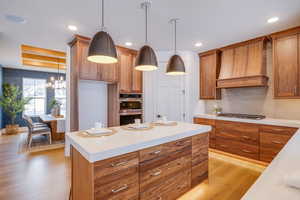 Kitchen with stainless steel appliances, light hardwood / wood-style floors, hanging light fixtures, and custom exhaust hood