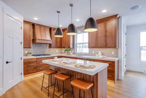 Kitchen featuring sink, a center island, hanging light fixtures, light wood-type flooring, and custom range hood