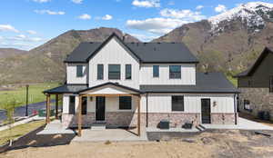 View of front of home with central AC, board and batten siding, a shingled roof, a mountain view, and brick siding