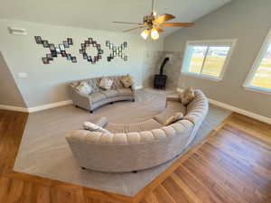 Family room featuring vaulted ceilings, a wood burning stove, plush carpet & a ceiling fan