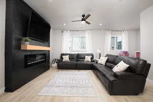 Living room featuring ceiling fan, a large fireplace, and light wood-type flooring