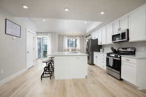 Kitchen with white cabinetry, appliances with stainless steel finishes, sink, and an island with sink