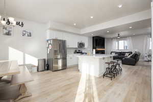 Kitchen with a breakfast bar, appliances with stainless steel finishes, an island with sink, white cabinets, and decorative light fixtures