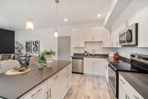 Kitchen with appliances with stainless steel finishes, decorative light fixtures, sink, white cabinets, and light wood-type flooring