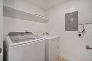 Clothes washing area featuring washing machine and clothes dryer, electric panel, and light hardwood / wood-style flooring