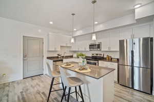 Kitchen featuring pendant lighting, sink, stainless steel appliances, white cabinets, and a kitchen island