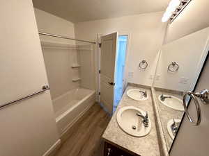 Full bath with wood finished floors, double vanity, a textured ceiling, and  shower combination