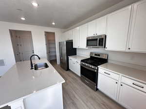Kitchen featuring appliances with stainless steel finishes, a sink, light wood finished floors, white cabinetry, and recessed lighting