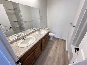 Bathroom featuring wood finished floors, double vanity, toilet, baseboards, and shower / tub combination