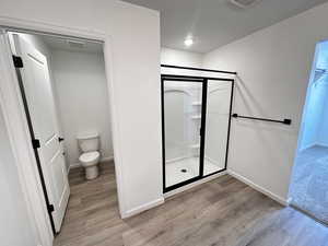 Full bath with a shower stall, wood finished floors, baseboards, and toilet
