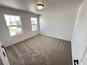 Empty room featuring a textured ceiling, carpet flooring, and baseboards