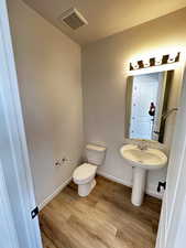 Half bath with toilet, wood finished floors, baseboards, and a sink