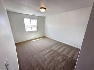 Carpeted empty room with a textured ceiling and baseboards