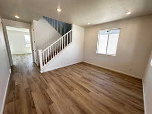 Unfurnished living room featuring wood finished floors, baseboards, stairway, recessed lighting, and a textured ceiling