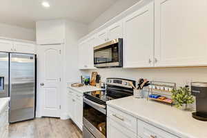 Kitchen with appliances with stainless steel finishes, white cabinets, and light hardwood / wood-style flooring