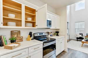 Kitchen with a high ceiling, white cabinetry, appliances with stainless steel finishes, and light hardwood / wood-style floors