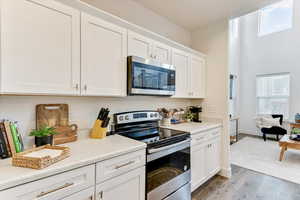 Kitchen featuring white cabinetry, a towering ceiling, stainless steel appliances, and light hardwood / wood-style flooring