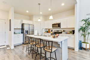 Kitchen with sink, white cabinetry, hanging light fixtures, appliances with stainless steel finishes, and an island with sink