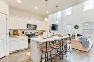 Kitchen with a center island with sink, stainless steel appliances, hanging light fixtures, and white cabinets