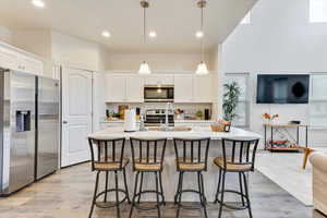 Kitchen with decorative light fixtures, white cabinetry, an island with sink, sink, and stainless steel appliances